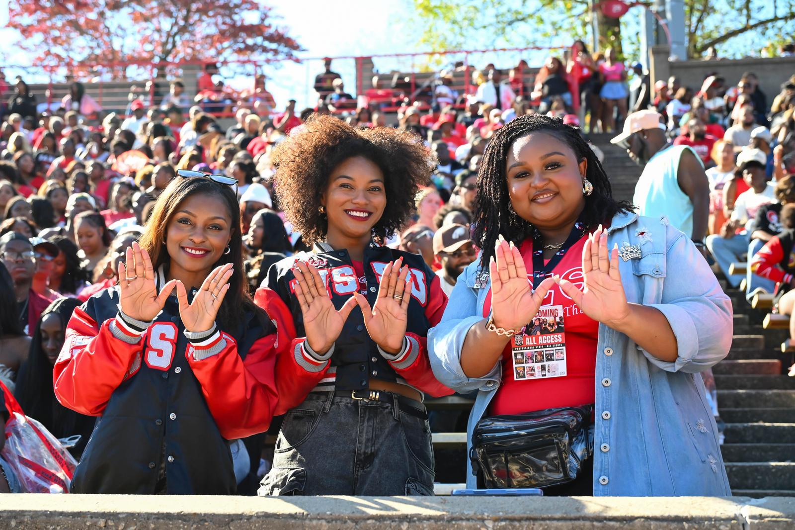 Three alumnae throwing the W hand sign at homecoming